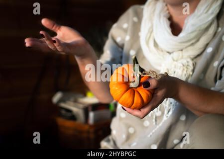 Eine Frau mit einem kleinen orangefarbenen Kürbis in den Händen. Vorderansicht. Stockfoto