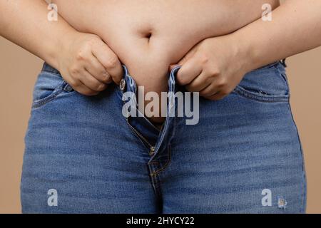 Übergewichtige Dame mit großem Bauch versucht, Reißverschluss Jeans der blauen Farbe. Viszerales Fett. Körper positiv. Plötzliche Gewichtszunahme. Enge Klamotten. Bedarf Stockfoto