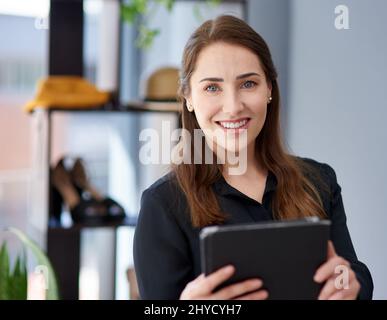 Mein Geschäft boomt auch online. Porträt einer jungen Geschäftsbesitzerin, die in ihrem Bekleidungsgeschäft ein digitales Tablet benutzt. Stockfoto