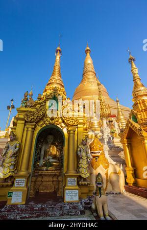 Kleine Pagoden und Statuen vor der vergoldeten Shwedagon Pagode in Yangon, Myanmar an einem sonnigen Tag. Stockfoto