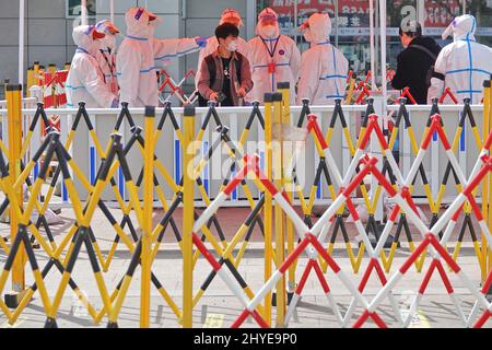 YANTAI, CHINA - 15. MÄRZ 2022 - Mitarbeiter zur Epidemien-Prävention führen ausreisende Passagiere zur Entnahme von Nukleinsäuretestproben am Yantai-Bahnhof in Stockfoto