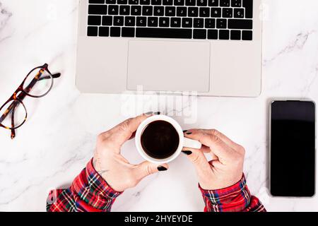 Draufsicht auf männliche Hände, die eine Tasse Kaffee halten, während sie an seinem Laptop arbeiten Stockfoto