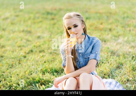 Porträt einer jungen Frau, die in einem Glas Orangensaft in einem Sommerpicknick im Park trinkt Stockfoto