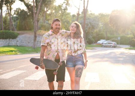 Junges cooles tätowierte Paar, das mit einem Skateboard zusammen läuft. Stockfoto