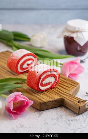 Hausgemachte rosa Cupcakes auf Holzbrett mit Frühlingszwiespeln und Glas Marmelade auf grauem Hintergrund Stockfoto