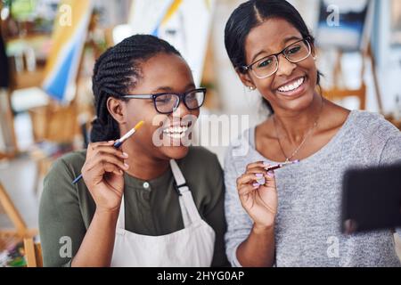 Sie werden so viel Freude daran haben, selbst etwas zu erschaffen. Ausgeschnittene Aufnahme von zwei jungen Frauen, die ein Selfie machen, während sie in einem Kunststudio malen. Stockfoto