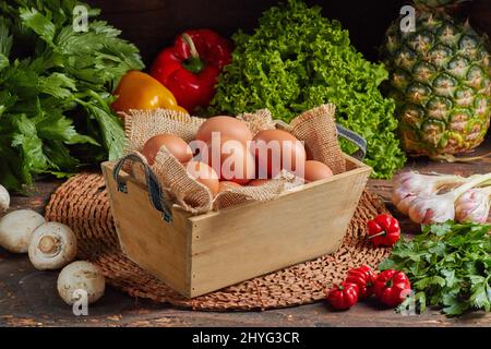 Schöne Schuss Eier in Holzkorb und Vielfalt an Gemüse und Obst auf einem Holztisch Stockfoto