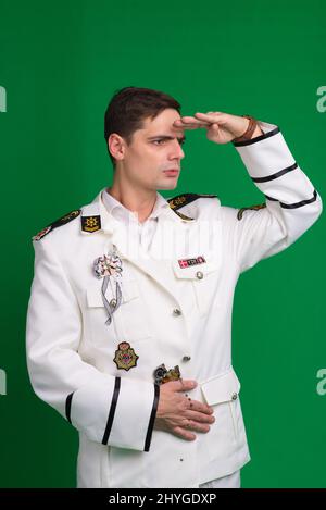 Ein Kapitän in einem weißen Anzug, halb gedreht stehend, isoliert auf grünem Hintergrund. Stockfoto