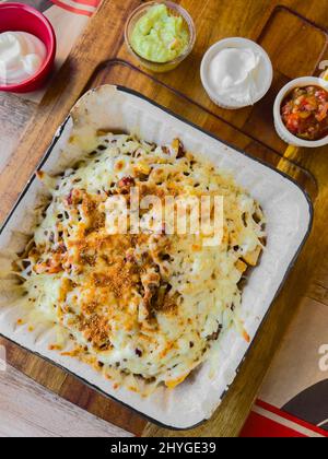 Nachos von Rind- und Cheddar-Käse auf Holzbrett mit Saucen an der Seite Stockfoto