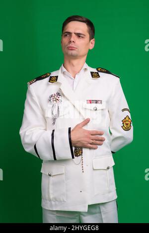 Ein Kapitän in einem weißen Anzug, halb gedreht stehend, isoliert auf grünem Hintergrund. Stockfoto