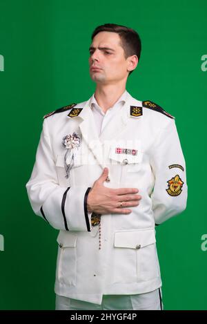 Ein Kapitän in einem weißen Anzug, halb gedreht stehend, isoliert auf grünem Hintergrund. Stockfoto
