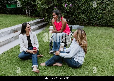 Lateinische Geschäftsfrau Transgender auf Rädern Stuhl und Freunde sitzen auf Gras und Spaß im Terrassenbüro in Mexiko Lateinamerika Stockfoto