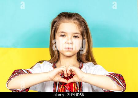 Ein Mädchen in ukrainischer Nationalkleidung, Wyschywanka, zeigt ein Herzzeichen als Zeichen der Liebe zur Ukraine. Stockfoto