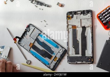 Repair of smartphones concept. Hand tool and disassembled phone lying on the table. Part of a series. Indoors. Selective focus. Stockfoto