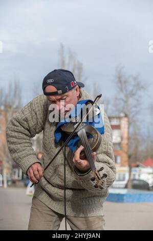 Straßenmusiker auf der elektronischen Geige. Ein reifer Mann mit schwarzer Baseballmütze und Audi-Logo. Ukraine, Nikolajew - 02 19 2022 Stockfoto