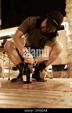 Vertikale Aufnahme eines asiatischen Mannes, der auf einer Straße eine Flasche Wein öffnet Stockfoto