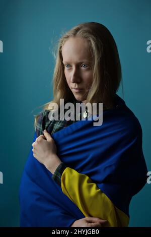 Eine echte ukrainische blonde Frau während des Krieges mit der staatlichen gelben und blauen ukrainischen Flagge auf ihrem Kopf. Russland griff die Ukraine am 24. Februar 2022 an. Stockfoto