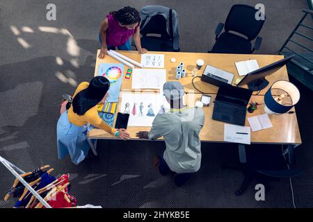 High-Angle-Ansicht von multirassischen jungen männlichen und weiblichen Modedesignern, die über Blaupausen diskutieren Stockfoto