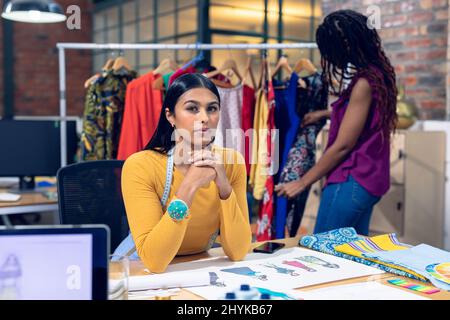 Portrait einer jungen Biracial-Modedesignerin am Schreibtisch und einer Mitarbeiterin im Hintergrund Stockfoto