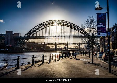 Tyne schlägt eine Brücke entlang des Kais in Newcastle upon Tyne, mit Sonne, die durch den Bogen und den blauen Himmel strömt Stockfoto