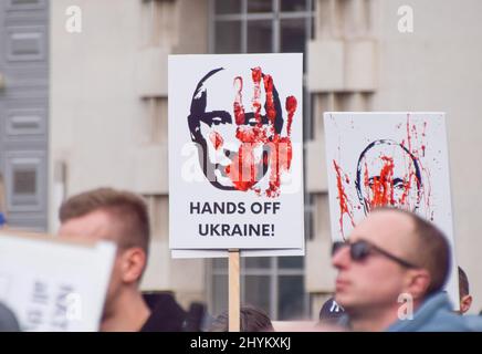 London, Großbritannien. 13.. März 2022. Ein Protestler hält ein Plakat mit Wladimir Putins Gesicht und den Worten „Hände weg von der Ukraine“. Demonstranten versammelten sich vor der Downing Street zur Unterstützung der Ukraine, während Russland seinen Angriff fortsetzt. Stockfoto