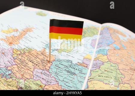 Die deutsche Nationalflagge ragt aus einer Nahaufnahme einer Karte oder eines Atlasses heraus, die sich auf Westeuropa konzentriert. Das Land Deutschland mit seinen Nachbarn. Stockfoto