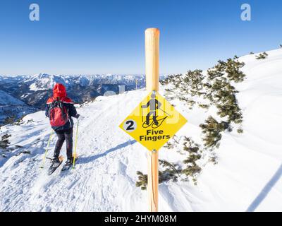 Blauer Himmel über der Winterlandschaft, Schneeschuhwanderer am Wegweiser auf Five Fingers Trail, Krippenstein, Salzkammergut, Oberösterreich, Österreich Stockfoto