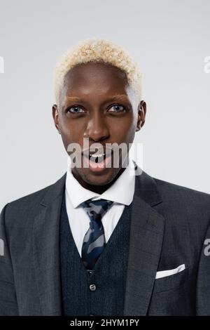 Porträt eines blonden und schockierten afroamerikanischen Mannes mit blauen Augen isoliert auf grau Stockfoto