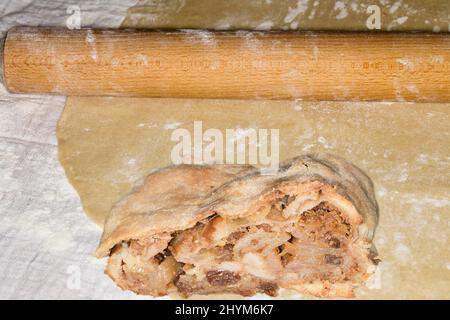 Auf einem Strudelteig liegen Nudelholz und ein Stück Apfelstrudel mit Sultanen Stockfoto