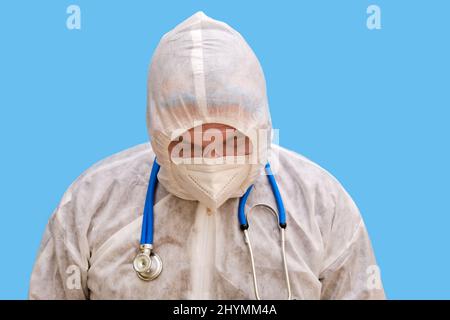 Mann Arzt Sanitäter in einem Schutzanzug Uniform mit Brille und Gesichtsmaske auf einem Studio blauen Hintergrund. Sanitäter in weißer antiviraler Schutzkleidung Stockfoto