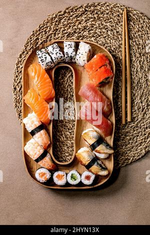 Sushi-Brötchen im Set. Traditionelles japanisches Sushi und Brötchen mit frischem Lachs, Thunfisch, Aal und Garnelen auf Reis. Servieren auf Holzplatte mit Essstäbchen auf Stockfoto
