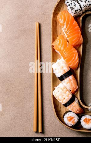 Sushi-Brötchen im Set. Traditionelles japanisches Sushi und Brötchen mit frischem Lachs, Thunfisch, Aal und Garnelen auf Reis. Servieren auf Holzplatte mit Essstäbchen auf Stockfoto