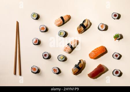 Sushi-Brötchen im Set. Traditionelles japanisches Sushi und Brötchen mit frischem Lachs, Thunfisch, Aal und Garnelen auf Reis, Holzkitzelwaren auf beigem Hintergrund mit Stockfoto