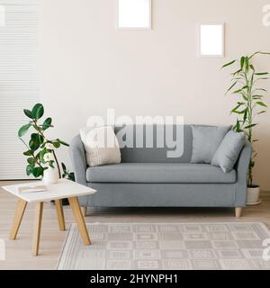 Das Interieur eines modernen Wohnzimmers in hellen Farben. Sofa mit Kissen, Couchtisch, Ficus und Bambus in einer Kanne, geschnitzte Holzwand mit geometrischem p Stockfoto