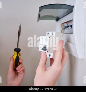 Eine Frau wechselt eine automatische Sicherung in einer Hauselektrik. Selbstreparatur und Austausch von elektrischen Geräten in der Wohnung, diy Stockfoto