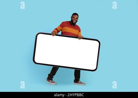 Mobile Werbung. Glücklich Jung Schwarz Männlich Trägt Big Blank Smartphone Stockfoto