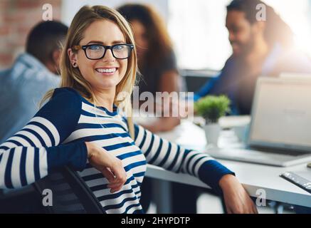 Haben Design immer aus frischen Perspektiven betrachtet. Porträt einer jungen Designerin, die im Büro mit ihren Kollegen im Hintergrund sitzt. Stockfoto