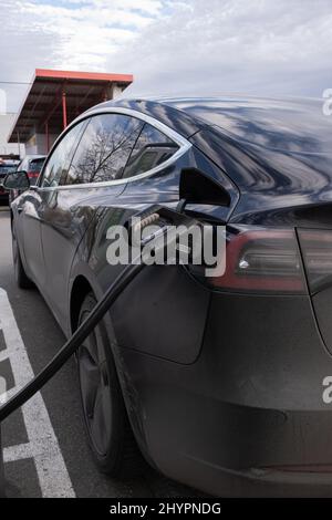 Tettnang, Deutschland - 18. Februar 2022: Eine statische Aufnahme eines soliden schwarzen Tesla Model 3 Dual-Motors, der auf der Kaufland Supermarkt DC-Ladestati geladen wird Stockfoto