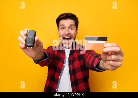 Aufgeregt Kerl Zeigt Auto-Schlüssel Und Kreditkarte, Gelber Hintergrund Stockfoto