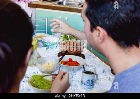 Rückansicht und Nahaufnahme des kaukasischen Paares, das gemeinsam das Mittagessen genießt und vegetarische und gesunde Speisen vom Tisch zum Essen nimmt. Stockfoto