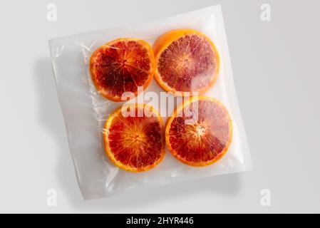 Vier Scheiben rote Orangen Früchte in Vakuum verpackt versiegelt für Sous-Vide Kochen isoliert auf grauem Hintergrund in der Draufsicht Stockfoto