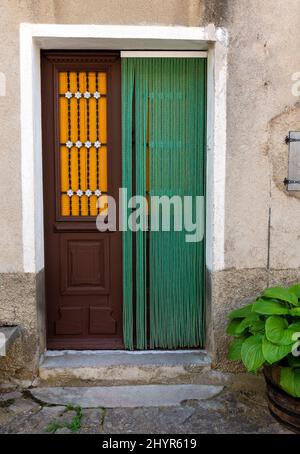 Die spanische Tür zeigt eine Holztür mit grünem Türvorhang und orangefarbenen Fensterläden Stockfoto