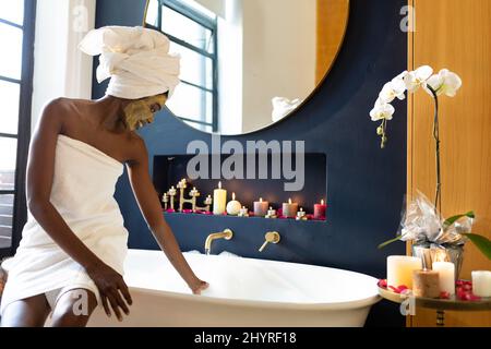 afroamerikanische Frau trägt Handtuch Herstellung Vorbereitung für Schaumbad in der Badewanne zu Hause Stockfoto