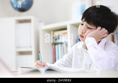 Ein Schüler, der von den aufgetürmten Hausaufgaben und dem mühsamen Studium erschöpft ist, lernt, indem er schwierige Probleme mit einem müden Blick löst. Stockfoto