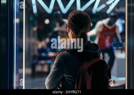 Frau steht vor dem Laden und schaut durch das Fenster nach innen Stockfoto