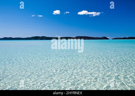 Kristallklares Wasser an einem wunderschönen Strand. Flaches Meerwasser mit Blick auf die Insel. Stockfoto