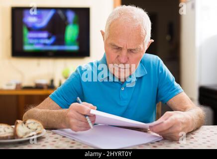 Fokussierter Senior beim Lesen und Unterzeichnen von Papieren am Tisch Stockfoto