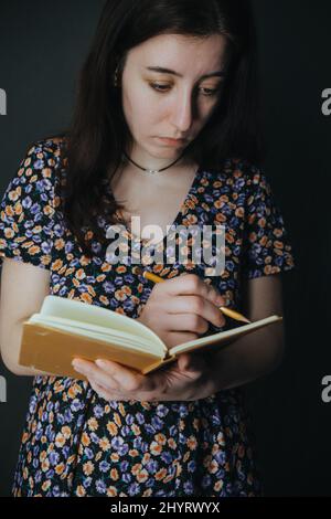 Die junge armenische ukrainerin notiert sich mit einem Stift in ihrem Notizbuch auf grauem Hintergrund Stockfoto