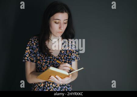 Die junge armenische ukrainerin notiert sich mit einem Stift in ihrem Notizbuch auf grauem Hintergrund Stockfoto