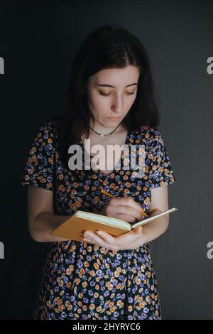 Die junge armenische ukrainerin notiert sich mit einem Stift in ihrem Notizbuch auf grauem Hintergrund Stockfoto